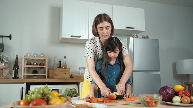 Madre intelligente e ragazza asiatica che cucinano insieme e tagliano le verdure pedagogia