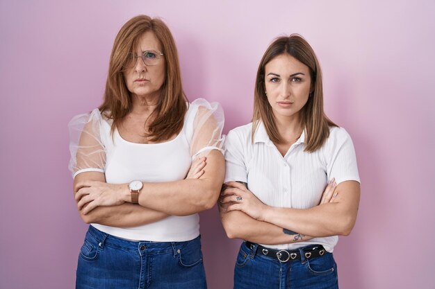 Madre ispanica e figlia che indossano una maglietta bianca casual su sfondo rosa espressione scettica e nervosa, di disapprovazione sul viso con le braccia incrociate. persona negativa.