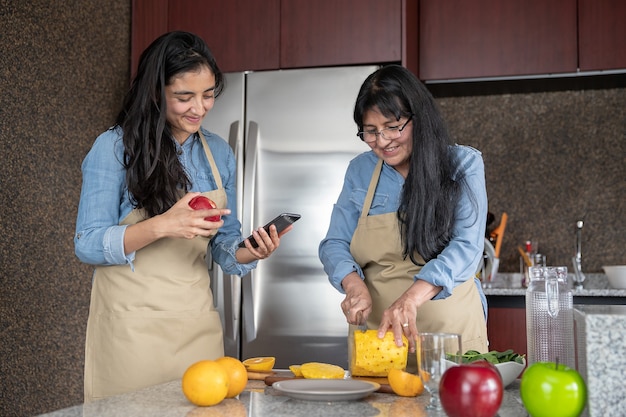 Madre messicana e figlia che cucinano in cucina guardando la ricetta sullo smartphone