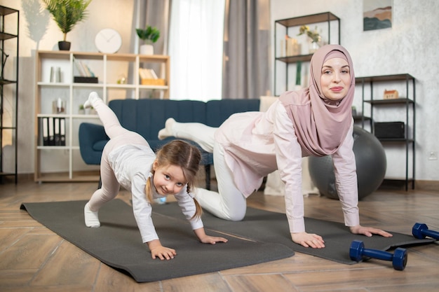 Madre musulmana e sua figlia fanno esercizio di fitness di stretching insieme a casa