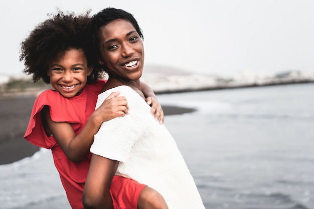 Madre nera e figlia che si divertono sulla spiaggia al tramonto durante le vacanze estive - Focus sul volto della madre