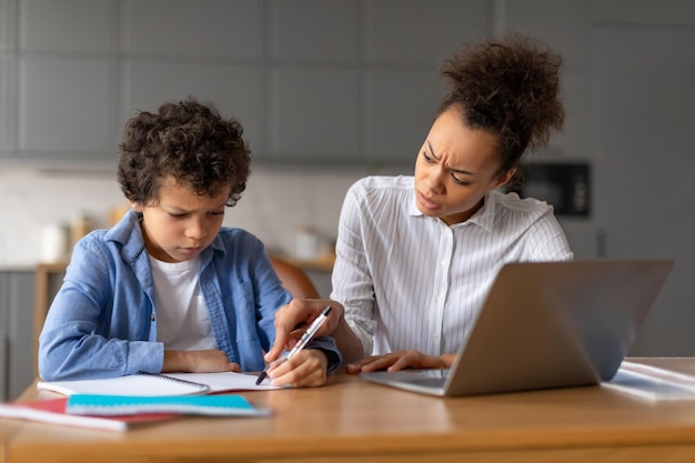 Madre nera preoccupata che aiuta il figlio concentrato con compiti difficili