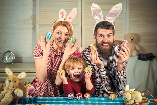 Madre, padre e figlio dipingono le uova. Buona Pasqua in famiglia. Piccolo bambino sveglio che porta le orecchie del coniglietto