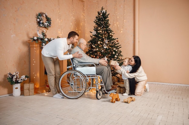 Madre padre figlio piccolo e vecchio nonno su una sedia a rotelle seduti vicino all'albero di Natale