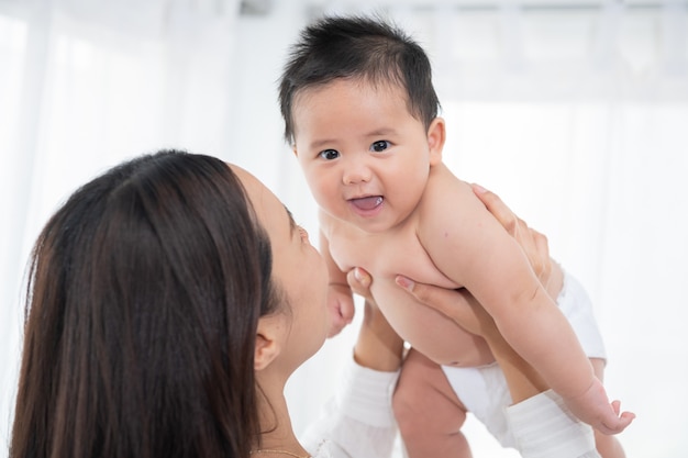 Madre ridente che solleva in aria il suo adorabile figlio neonato