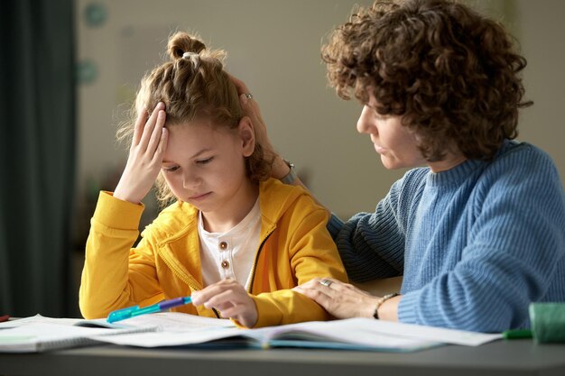 Madre seduta alla scrivania insieme a suo figlio e che gli spiega il materiale scolastico