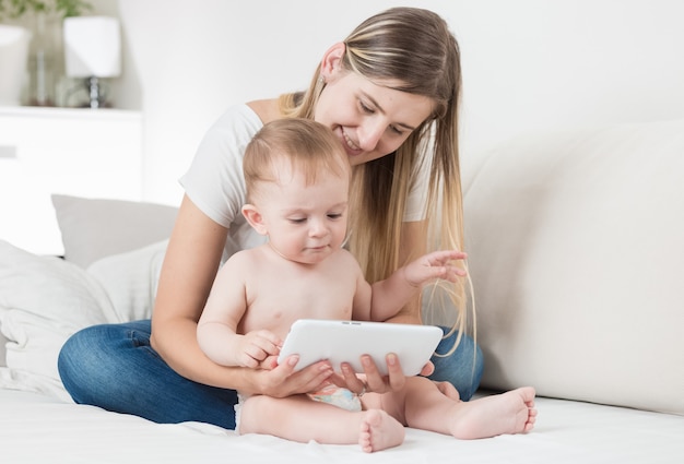 Madre seduta sul divano con il suo bambino e navigando in internet su tablet PC