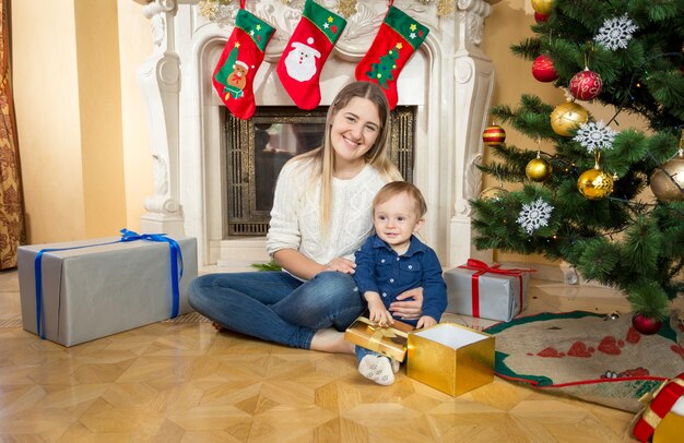 Madre seduta sul pavimento con il figlio bambino in soggiorno decorato per Natale