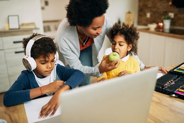 Madre single nera che dà ai suoi figli una mela per uno spuntino durante l'homeschooling