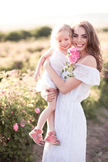Madre sorridente che tiene in braccio una bambina in un campo di rose