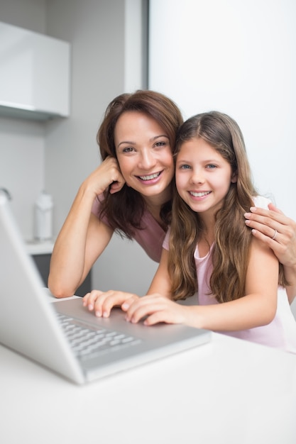 Madre sorridente con la figlia che utilizza computer portatile nella cucina