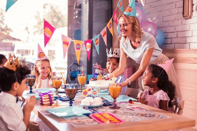 Madre sorridente e portando la torta di compleanno per i bambini