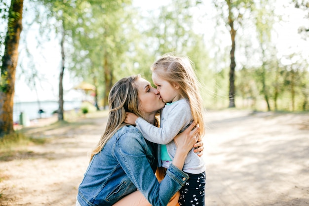 Madre sorridente felice che bacia la sua piccola figlia adorabile all'aperto