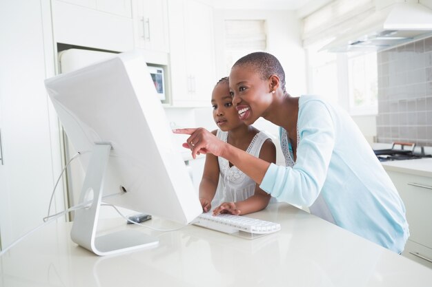 Madre sorridente felice con sua figlia che per mezzo del computer