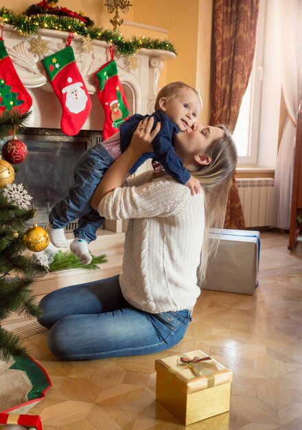 Madre sorridente felice e figlio del bambino di 1 anno che posano all'albero di Natale