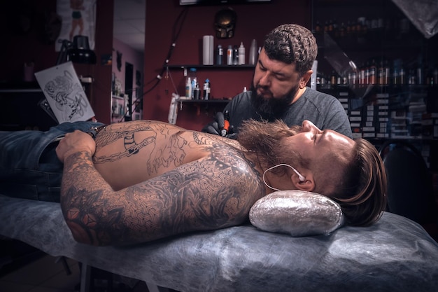 Maestro del tatuaggio che fa arte del tatuaggio in studio./Tatuatore che mostra il processo di realizzazione di un tatuaggio nel salone del tatuaggio.
