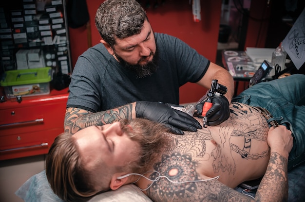 Maestro del tatuaggio che fa tatuaggio nello studio del tatuaggio. Artista del tatuaggio che fa arte del tatuaggio nel suo salone.