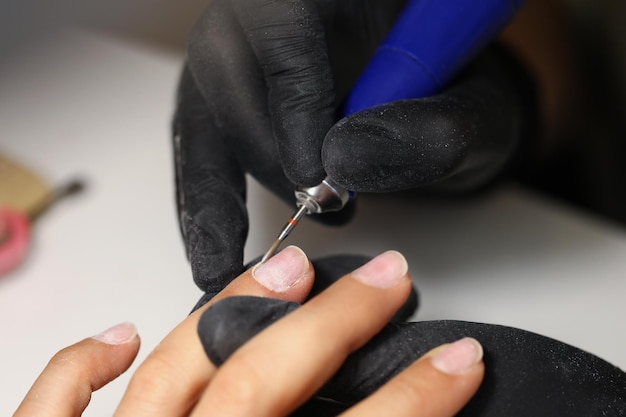 Maestro delle unghie che utilizza uno strumento per pulire le unghie delle clienti femminili nello studio di bellezza
