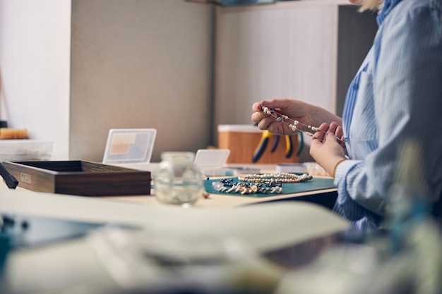 Maestro di bigiotteria che tiene una collana alla moda con perle sul posto di lavoro