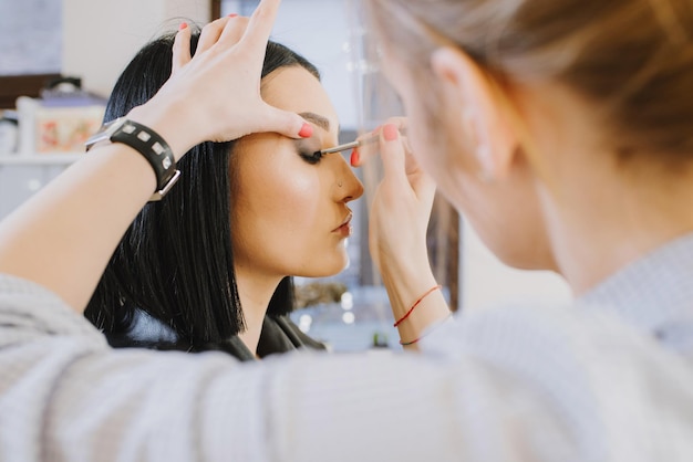 Maestro di trucco che fa il trucco al bellissimo studio di bellezza al coperto del modello