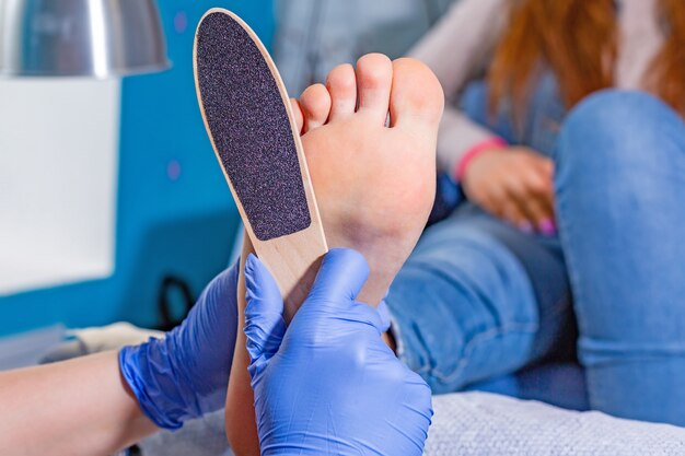 Maestro durante una pedicure. Il processo di pedicure professionali. Il mago nella maschera provoca il gel sulle unghie con un pennello. Il concetto di bellezza e salute