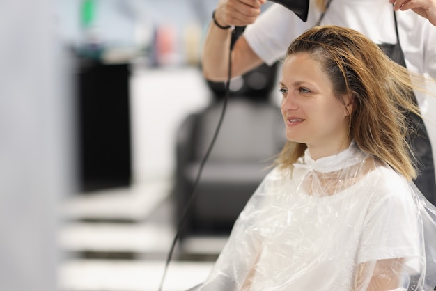 Maestro parrucchiere asciuga i capelli con asciugacapelli a cliente nel salone di bellezza