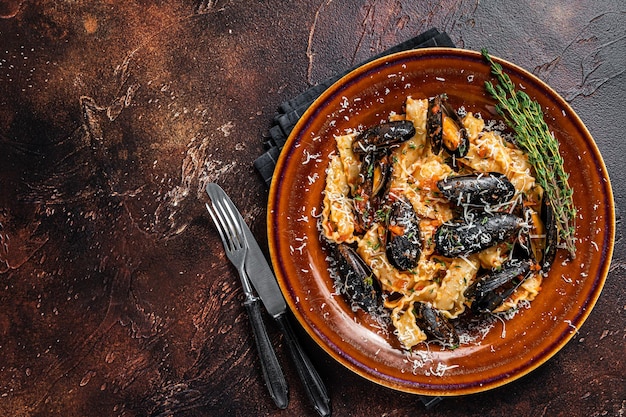 Mafaldine di mare con cozze e salsa di pomodoro in un piatto rustico. Sfondo scuro. Vista dall'alto. Copia spazio.