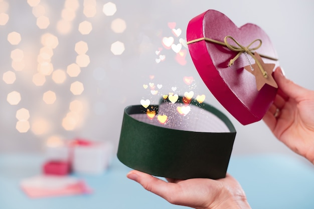 Magia per San Valentino, regali in scatola aperta a forma di cuore nelle mani. Copi lo spazio per il messaggio di amore. Scegli il regalo di Natale per la persona amata, il primo piano, il bokeh del cuore e la polvere.