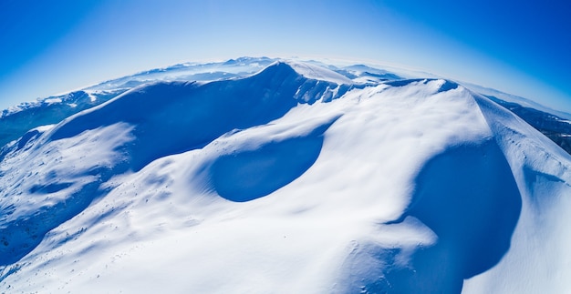Magico panorama di una bellissima collina tra le montagne coperte di neve sulla pista da sci in una giornata di sole con un cielo blu chiaro. Concetto di turismo invernale. Copyspace
