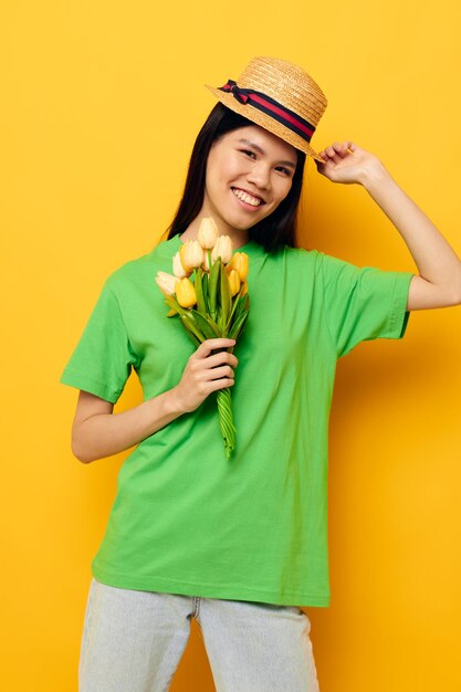 Maglietta verde graziosa del brunette un mazzo dei fiori gialli in un fondo isolato del cappello inalterato