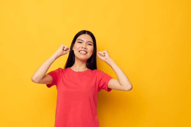 Magliette rosse affascinanti della giovane donna asiatica che posano il fondo giallo di stile moderno inalterato