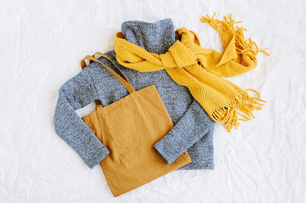 Maglione blu con sciarpa lavorata a maglia gialla e tote bag. Collage di vestiti di moda autunno/inverno su sfondo bianco. Vista dall'alto piatta.