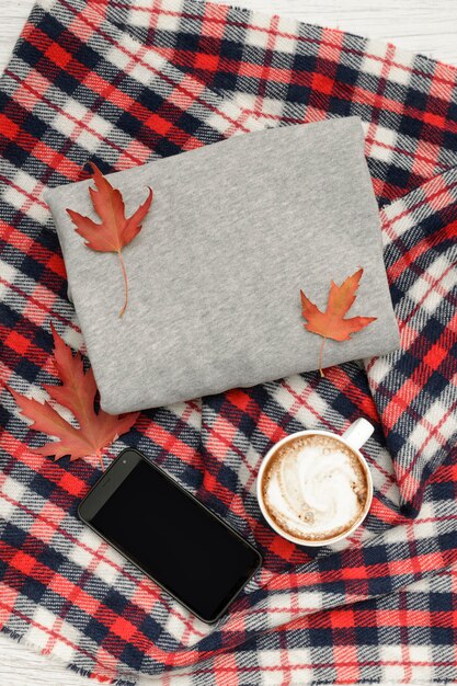 Maglione grigio, plaid, tazza da caffè e smartphone. Foglie d'autunno