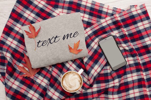 Maglione grigio, plaid, tazza di caffè e smartphone. Foglie d'autunno. Concetto alla moda