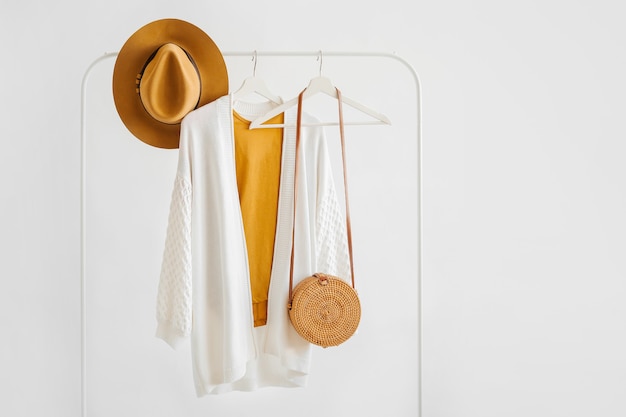 Maglione lavorato a maglia bianco su appendiabiti con cappello marrone e borsa di bambù