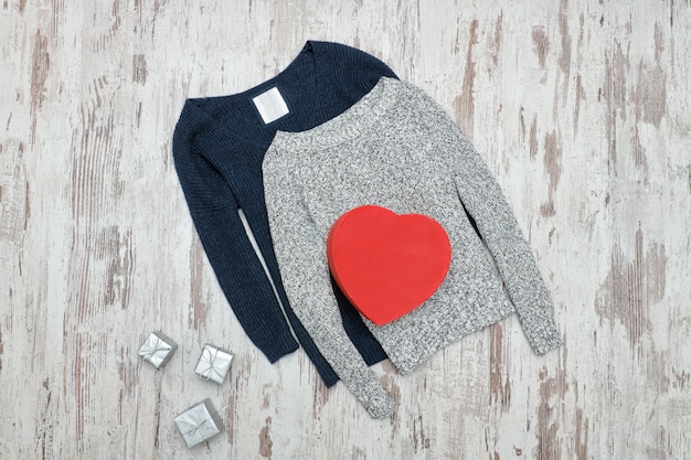 Maglione lavorato a maglia grigio e blu. Scatole regalo a forma di cuore in argento e rosso. Concetto alla moda