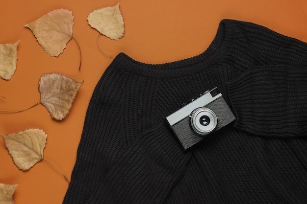 Maglione nero con una fotocamera retrò e foglie cadute