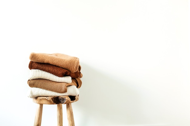 Maglioni lavorati a maglia di lana femminili caldi di inverno, pila di pullover sullo sgabello di legno al bianco. Concetto di vestiti moderni per riviste, blog, social media.