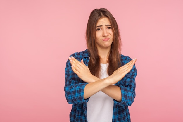 Mai più. Ritratto di una ragazza delusa sconvolta con una camicia a scacchi che incrocia le mani, mostrando un gesto di negazione dell'arresto, dicendo di no definitivo, questa è la fine. studio indoor girato isolato su sfondo rosa