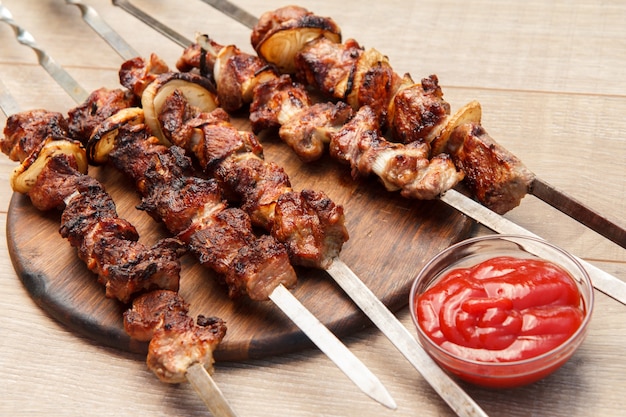 Maiale alla griglia su spiedini arrosto alla griglia su tagliere di legno con salsa di pomodoro in una ciotola. Barbecue, picnic