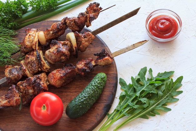 Maiale alla griglia su spiedini di metallo con erba cipollina fresca di aneto di rucola e prezzemolo su tagliere di legno