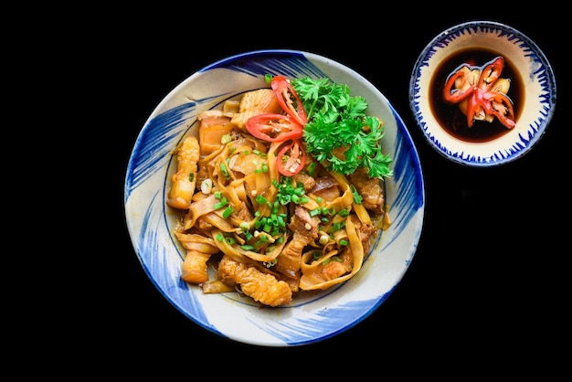 Maiale fritto vietnamita con noodle e zenzero su sfondo nero
