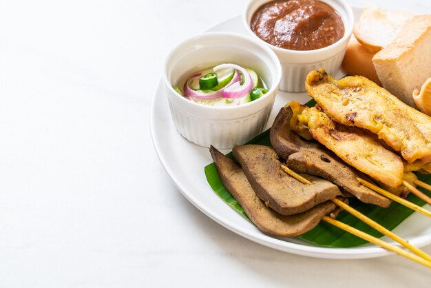 Maiale Satay con salsa di arachidi e sottaceti che sono fette di cetriolo e cipolle in aceto