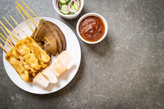 Maiale Satay con salsa di arachidi e sottaceti che sono fette di cetriolo e cipolle in aceto