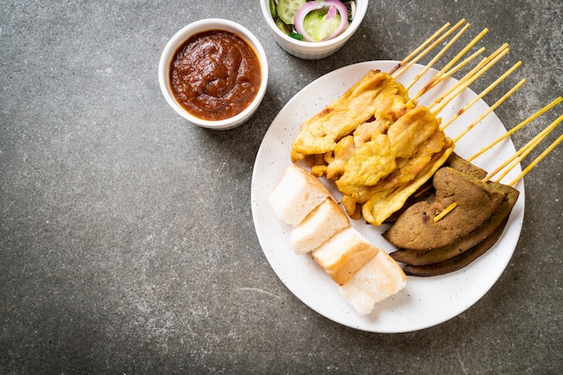 Maiale Satay con salsa di arachidi e sottaceti che sono fette di cetriolo e cipolle in aceto