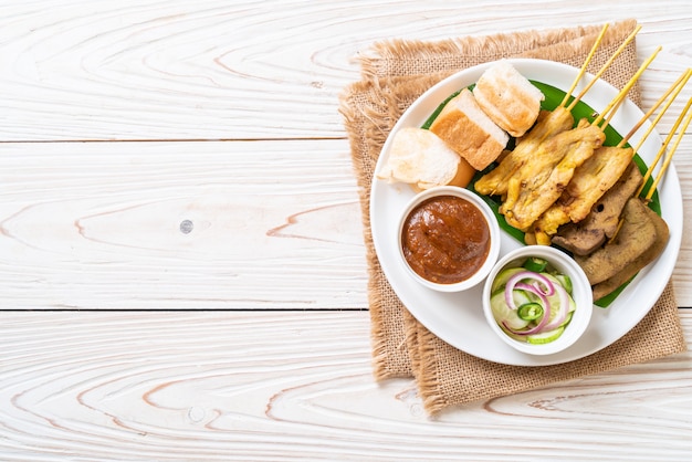 Maiale Satay con salsa di arachidi e sottaceti che sono fette di cetriolo e cipolle in aceto