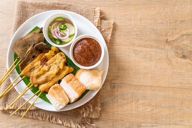 Maiale Satay con salsa di arachidi e sottaceti che sono fette di cetriolo e cipolle in aceto