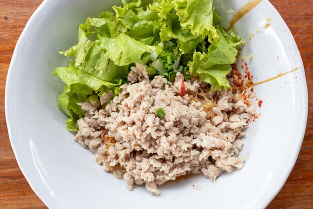 Maiale tritato piccante tailandese con le tagliatelle all'uovo servito su una tavola di legno rustica.