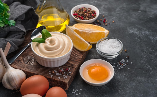 Maionese fresca su uno sfondo scuro con ingredienti per la sua preparazione. Maionese fatta in casa. Vista laterale.