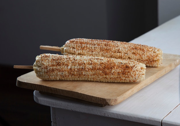 Mais bianco bollito messicano sulla pannocchia con peperoncino lime e maionese sul tavolo di legno